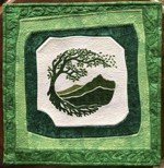 A small wall quilt in green colors with the embroidered green tree in the center.