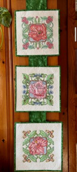 3 small quilts arranged on a background ribbon into a hanging.