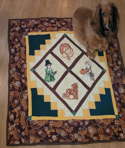 Thanksgiving quilt with embroidery of Pilgrim boy and girl, cornucopia and pumpkin.