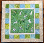 A small wall quilt for a nursery with embroidery of bunnies and dandelions in the central part, with 3 borders , all in green and blue shades.