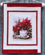 A small re-and-white wall quilt with embroidery of poinsettias and a cup of coffee.