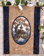 Small wall quilt with embroidery of a fairy cottage in the center.