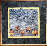 Small wall quilt with embroidered clouds and fall trees.