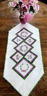 Light colored quilted tablerunner with flower embroidery in pink and green hues.