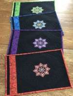 4 black placemats with embroidery in jewel tones.