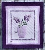 Wall quilt in lilac colors with lilac embroidery in a vase.