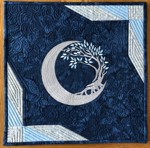 Small dark blue quilt with embroidery of a moon and tree in silver threads.