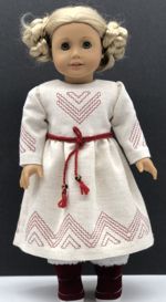 A doll in a light dress with Scandinavian style redwork embroidery.