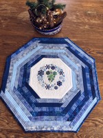 Quilted octagonal tabletopper made of blue scrap fabrics and snowflake embroidery in the center.