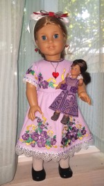 A 18-inch doll in a dress with flower embroidery holding a mini doll in a lace dress