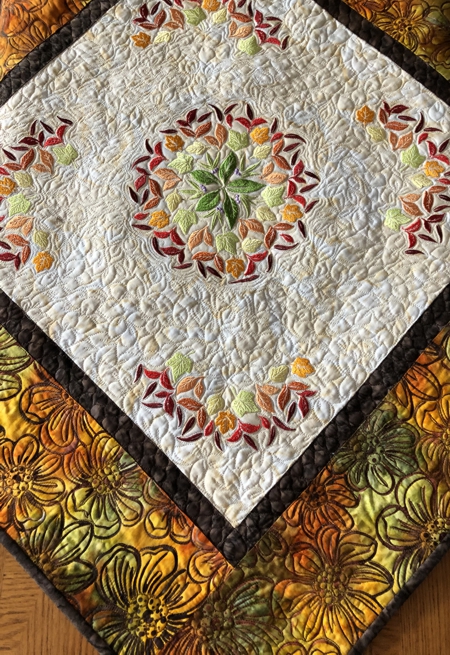 Finished quilted tabletopper featuring leaf embroidery in the central part. Close-up of the central part.