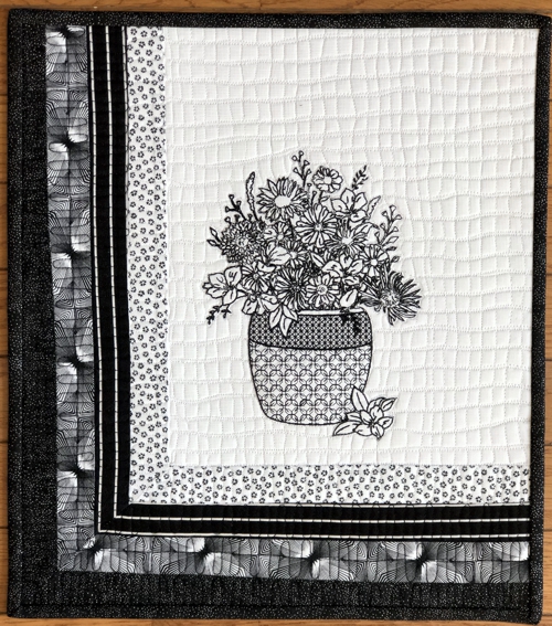Finished quilt with black embroidery on the white background. The left and lower borders are pieced using 4 black-and-white fabrics. Black binding.