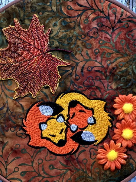 Close-up of the sleeping foxes stitch-out decorated with a leaf embroidery and silk flowers.