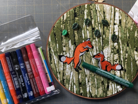 Sew on leaf buttons over the foxes. With green marker draw some grass under the foxes.