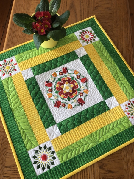 FInished small quilt in yellow and green colors with flower embroidery used as a tabletopper.