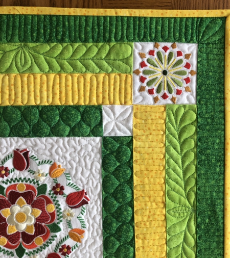 Detail of the finished small quilt in yellow and green colors with flower embroidery.