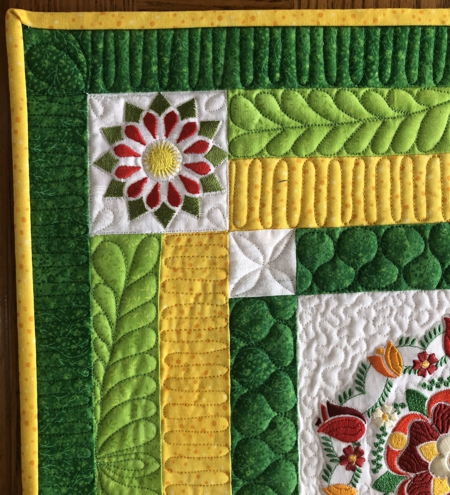 Detail of the finished small quilt in yellow and green colors with flower embroidery.