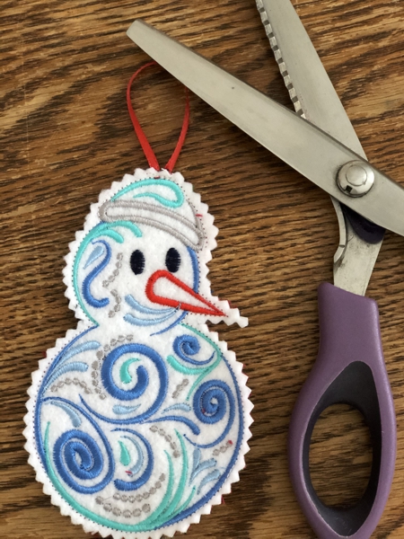 A finished snowman ornament with a pair of shears.