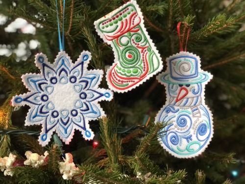 Finished ornaments of a stocking, snowman and a snowflake on a tree.