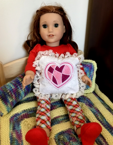 A doll holding the finished pillow with heart embroidery.