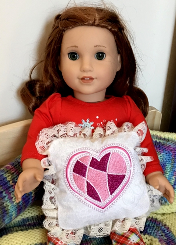 A doll with the small pillow with heart embroidery.