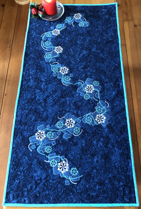 Finished tablerunner. Dark blue with snowflake-like embroidery.