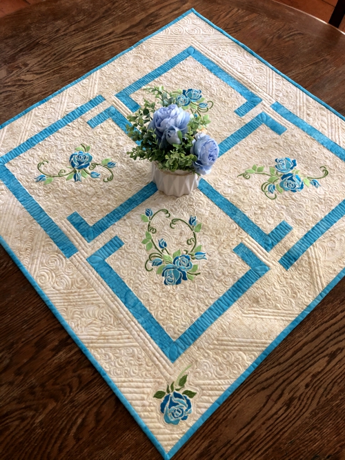 FInished tabletopper with blue roses embroidery.