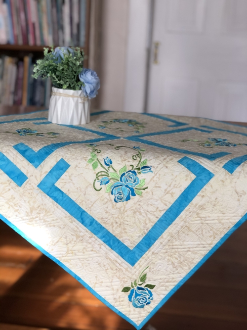 Finished tabletopper on a table with a vase of blue roses.