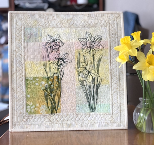 Finished quilt with daffodil embroidery and watercolor background pieced of different fabrics of pale hues.