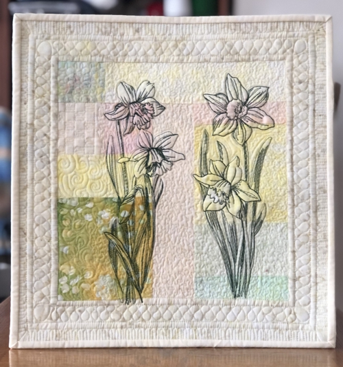 Finished quilt with daffodil embroidery and watercolor background pieced of different fabrics of pale hues.