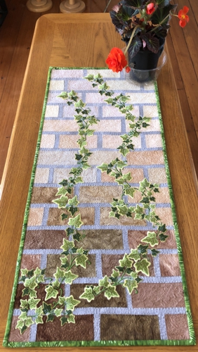 Finished quilt with ivy embroidery used as a tablerunner.