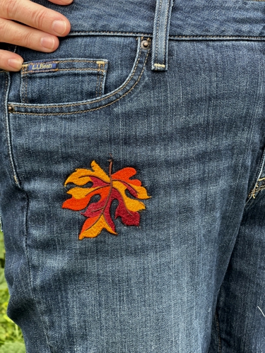 Jeans embellished with leaves embroidery. Close-up.