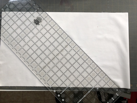 A strip of fabric folded in half with a quilters rules placed diagonally over it..