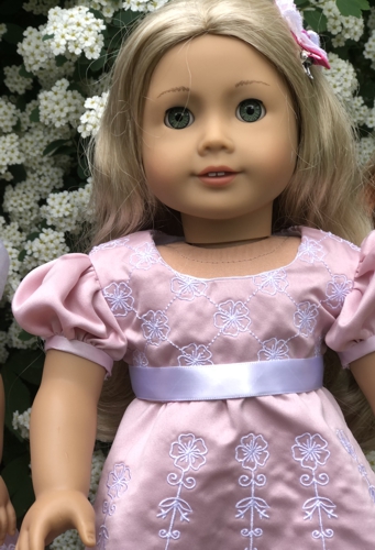A doll in pink dress with embroidery right on the fabric of the dress.