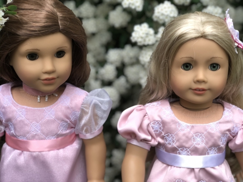 Two pink dresses on dolls with embroidered bodice.