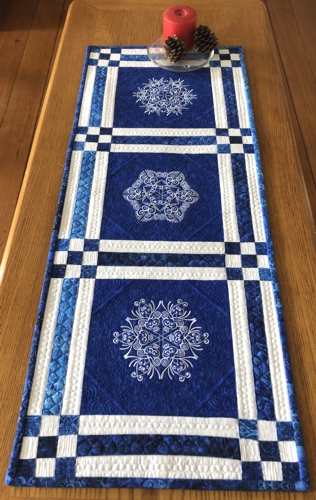 Finished quilted tablerunner with snowflake embroidery on a table.
