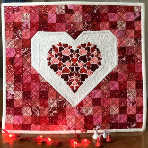 FInished wall quilt with embroidered heart in the center .