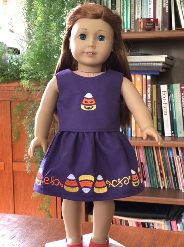 A doll in finished skirt and top with embroidery on bodice and skirt hem.