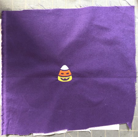 A stitch-out of a candy corn kernel on purple fabric