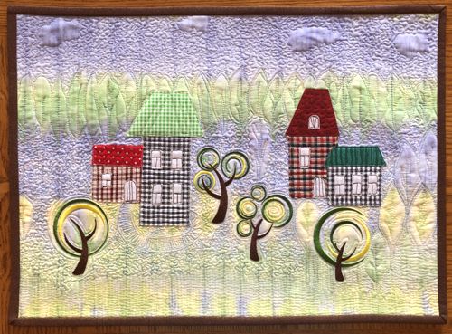 FInished quilt with gingham houses and embroidered trees.