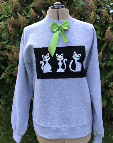 A grey sweatshirt with cat embroidery over a black background