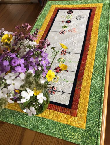 Finished tablerunner on a table with a bouquet of flowers.