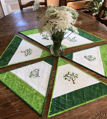 Finished quilted placemats with trees and butterflies embroidery on a table with a vase and flowers