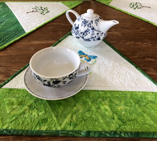 A close-up of a placemat with a butterfly embroidery served with a cup of tea and a tea pot