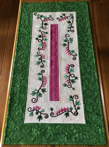 Quilted tablerunner with embroidery of bleeding heart flowers.