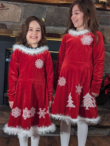 2 little girls in red dresses decorated with white Christmas-themed embroidery