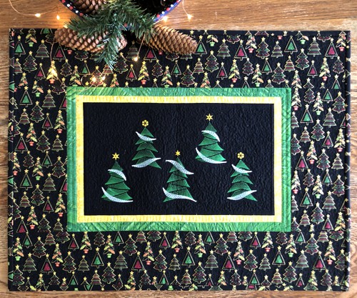 Small Christmas-themed wall quilt with embroidered fir trees on the black background and patterned borders.