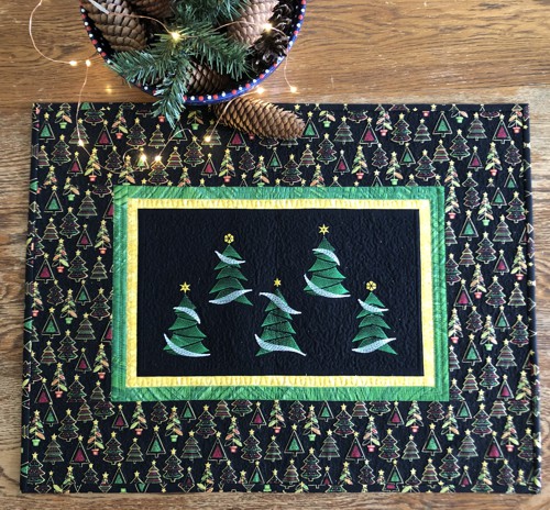 A finished Christmas-themed wall quilt with embroidery of fir-trees in the center and wide patterned borders.
