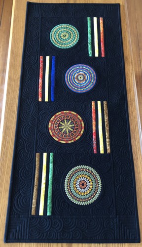 Quilted black tablerunner with embroidery of circle motifs in bright colors.
