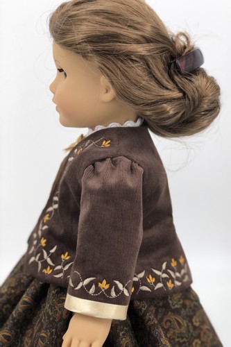 A doll in brown cordiroy jacket with embroidered bodice and sleeves. Side view.